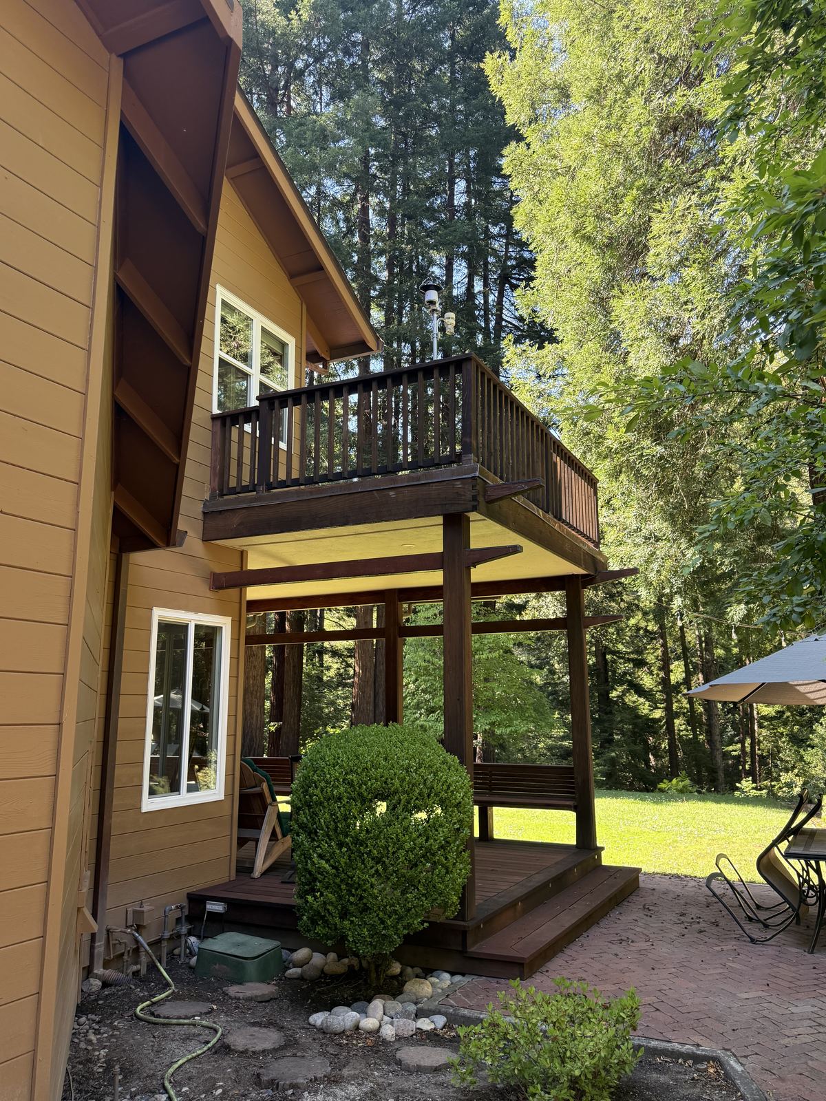 Second-story wood deck on posts with exposed underside, gas meter and shrub at the base