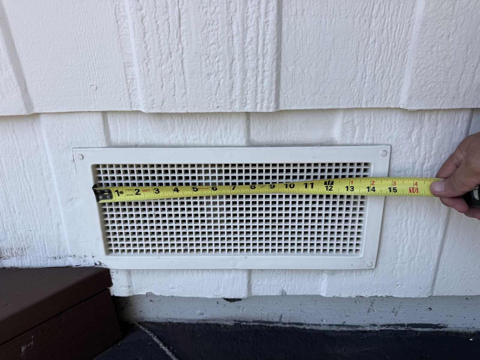 Plastic grid foundation vent being measured with a tape measure