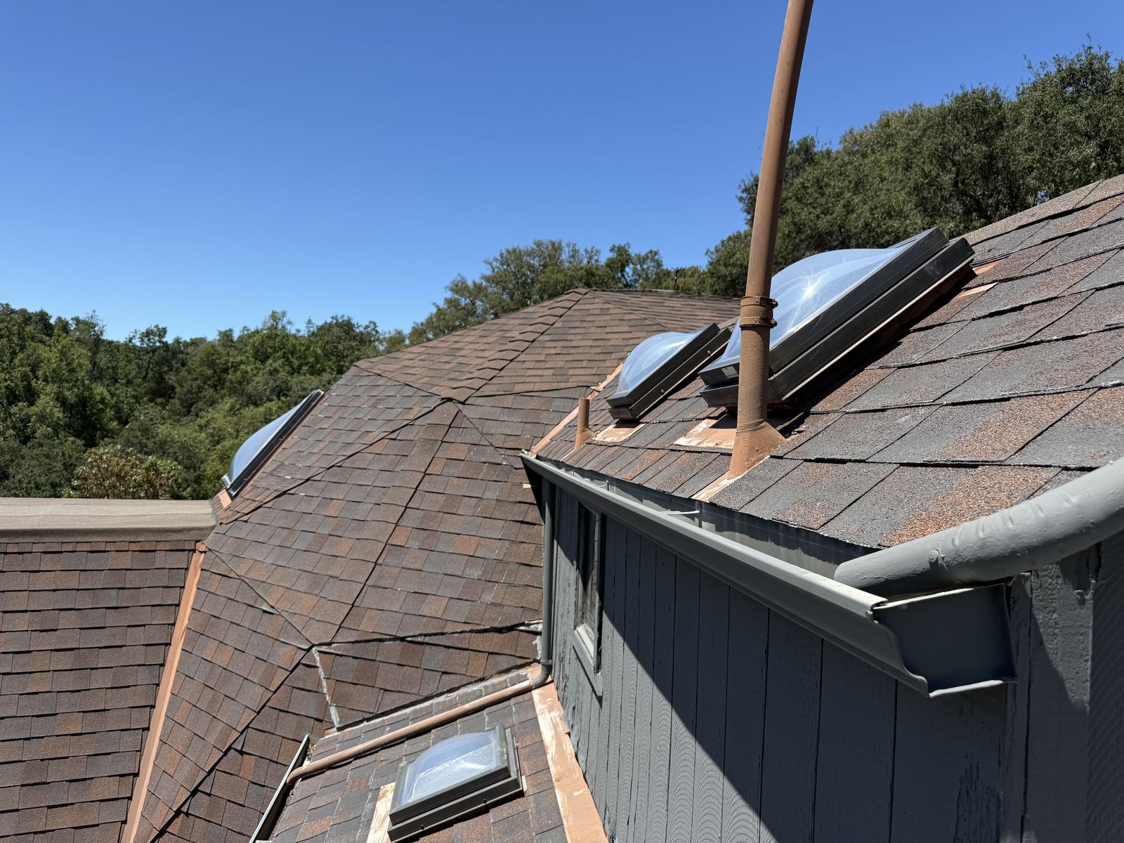 Rooftop view of a shingle roof with dome skylights and freshly sealed pipe penetrations
