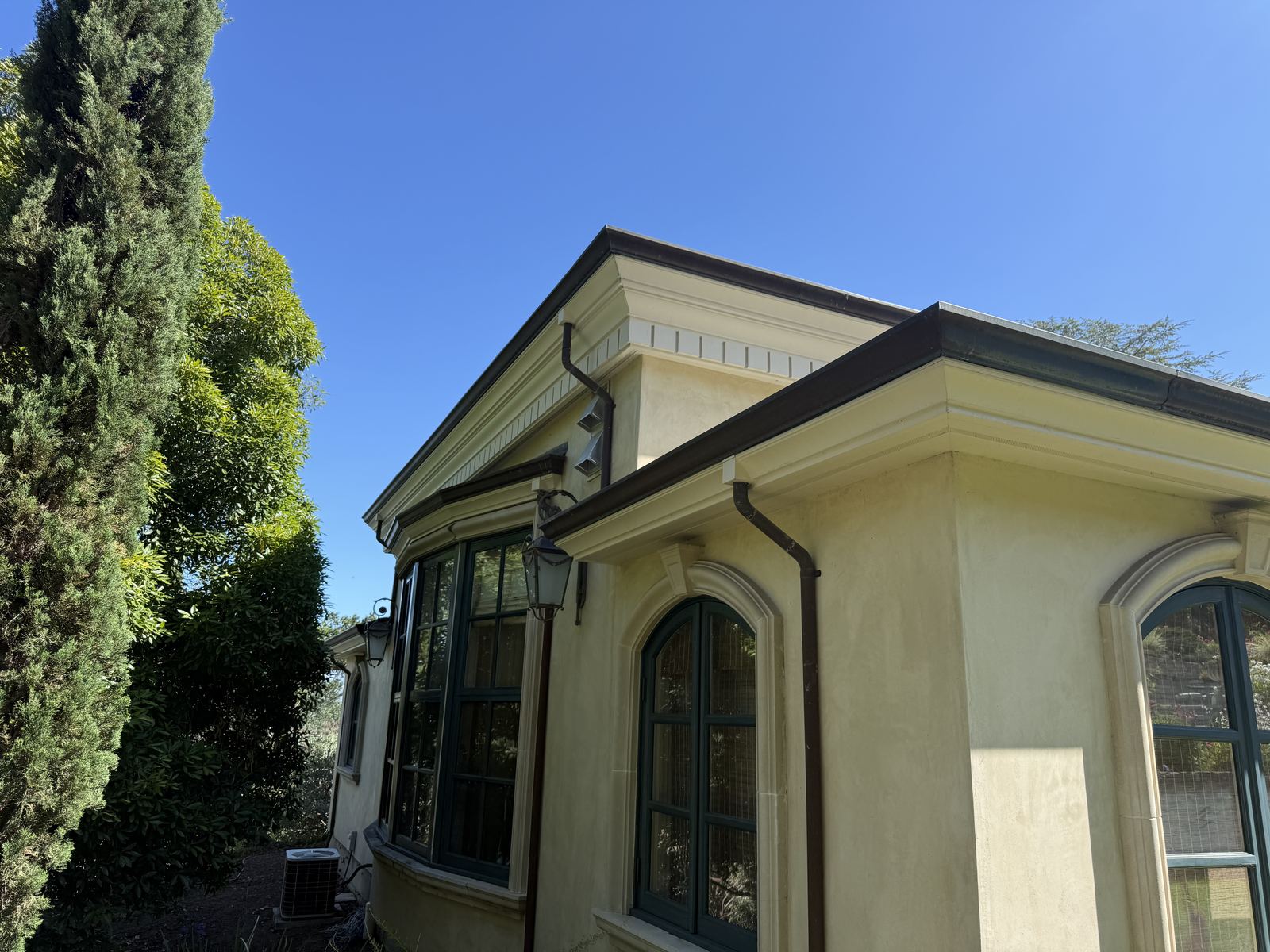 Stucco home with arched windows and dark metal roof edge, tall cypress close to the structure
